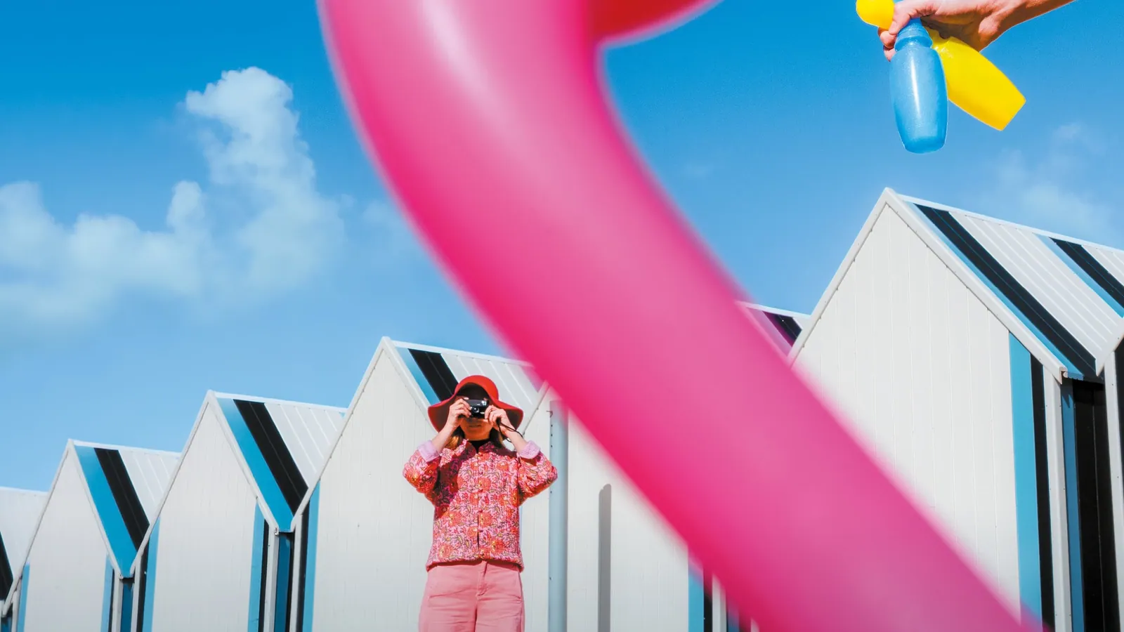Affiche 2026 : un flamant rose gonflable devant des cabines de plage, une photographe en rose au premier plan.